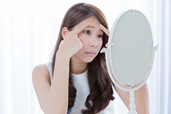 鏡で自身の顔のしわを確認する女性